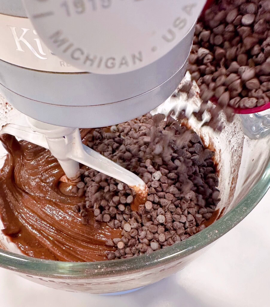 Adding in mini and regular chocolate chips to cake batter in the mixing bowl.