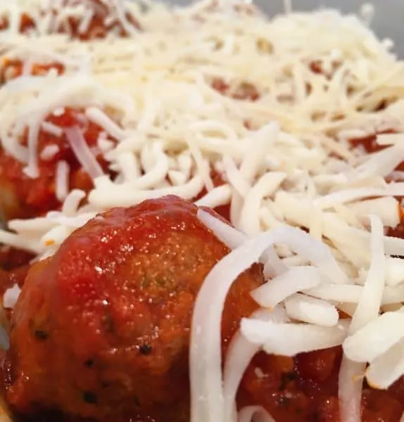Topping shells and sauce and meatballs with grated cheese.