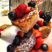 Heart shaped french toast with strawberries, blueberries and cream drizzled all over
