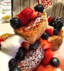 Heart shaped french toast with strawberries, blueberries and cream drizzled all over