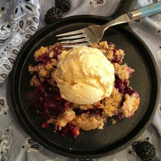 Triple Berry Cobbler serving on  a cast iron skillet with a big scoop of vanilla ice cream.