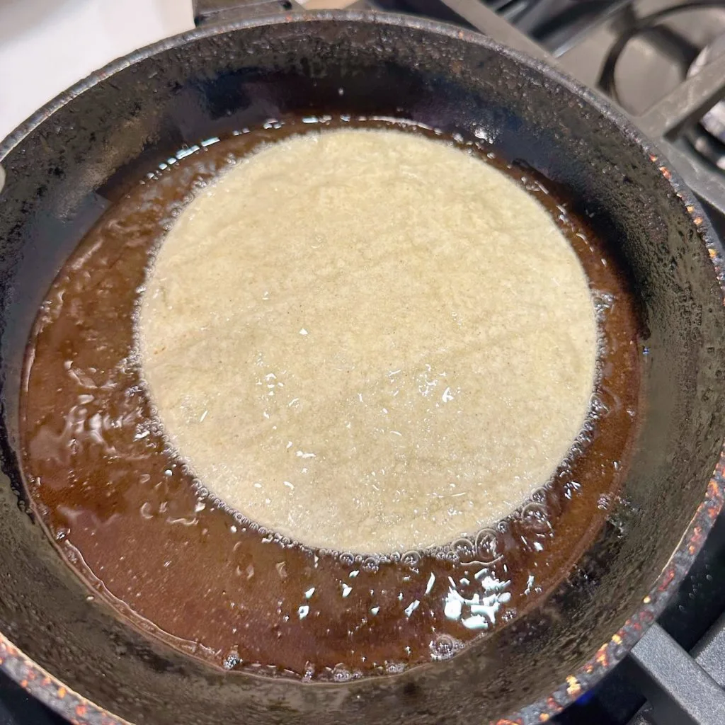 Corn tortillas in hot oil in a small fry pan on the stove top.
