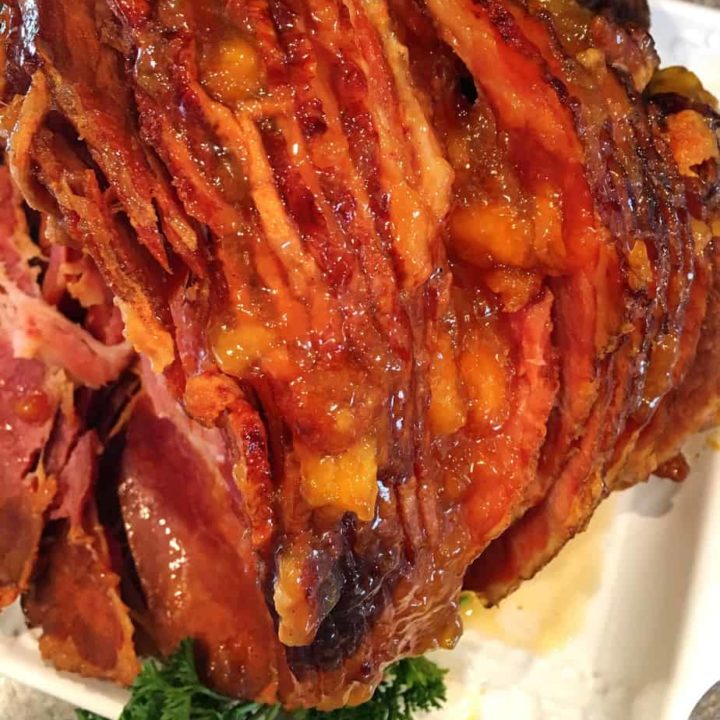 Spiral cut ham with a peach glaze on a white serving platter.