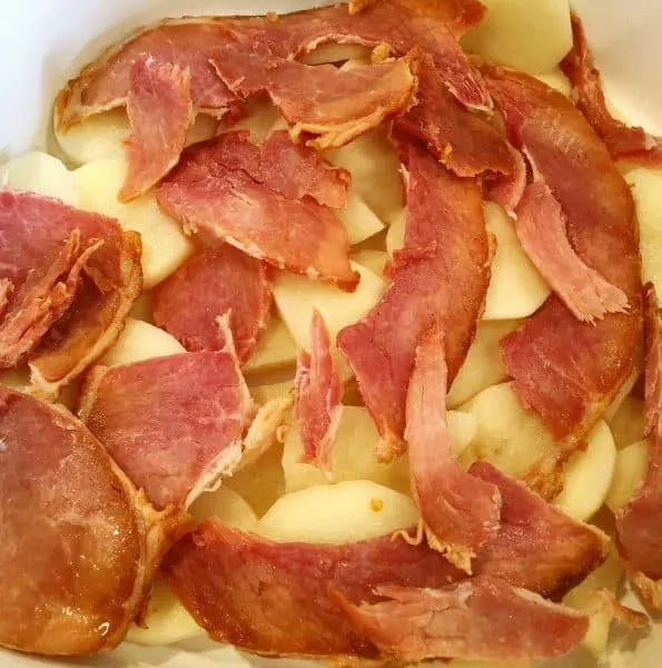 Layering sliced potatoes, ham, and white sauce in casserole dish