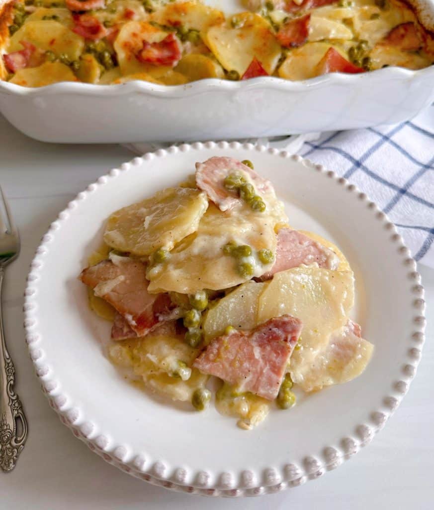 Serving of Ham and Potato casserole with the casserole in the background.