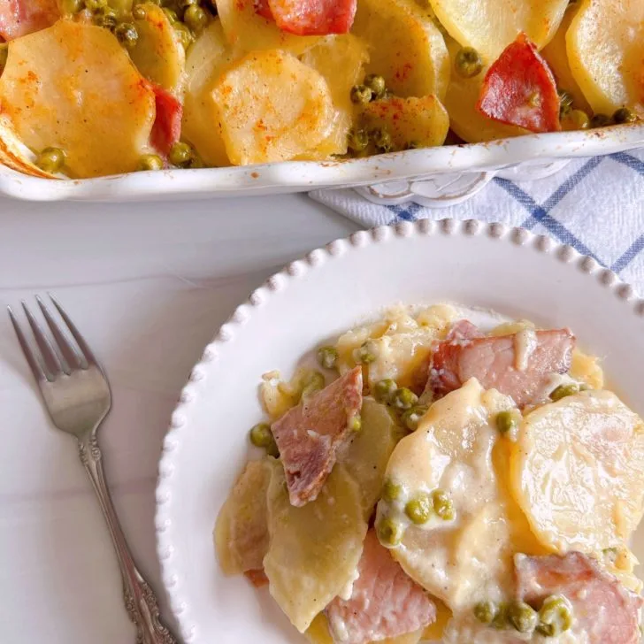 Creamy Ham, Pea, and Potato Casserole with a serving on a plate and the whole casserole in the background.
