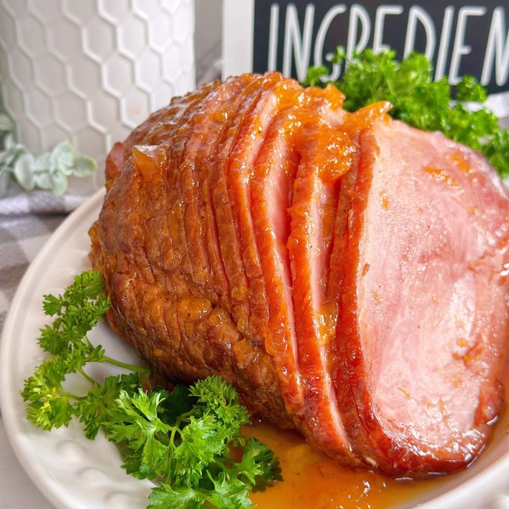 Spiral slow cooked peach-glazed ham on a white serving platter with parsley garnish.