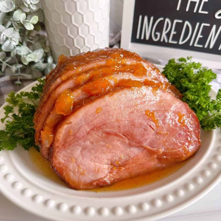 Slow Cooker Peach Glazed ham on a white platter surrounded by fresh parsley for garnish.
