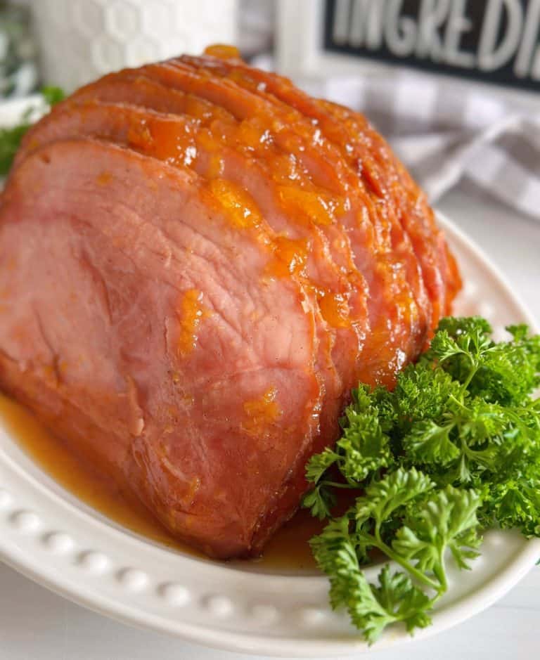 Peach Glazed Slow Cooker ham on a serving platter with fresh sprigs of parsley.