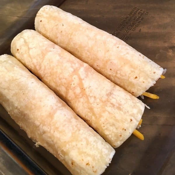 Rolled chicken enchiladas in casserole dish.