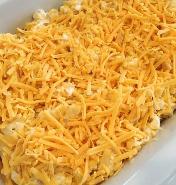 Cheese sprinkled on top of cheesy funeral potatoes before baking