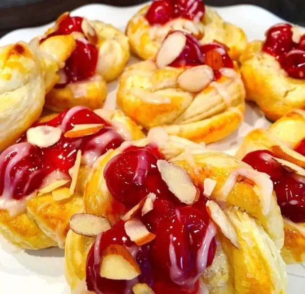 add cherry pie topping on top of cheesecake filling with sweet frosting drizzle and slivered almonds