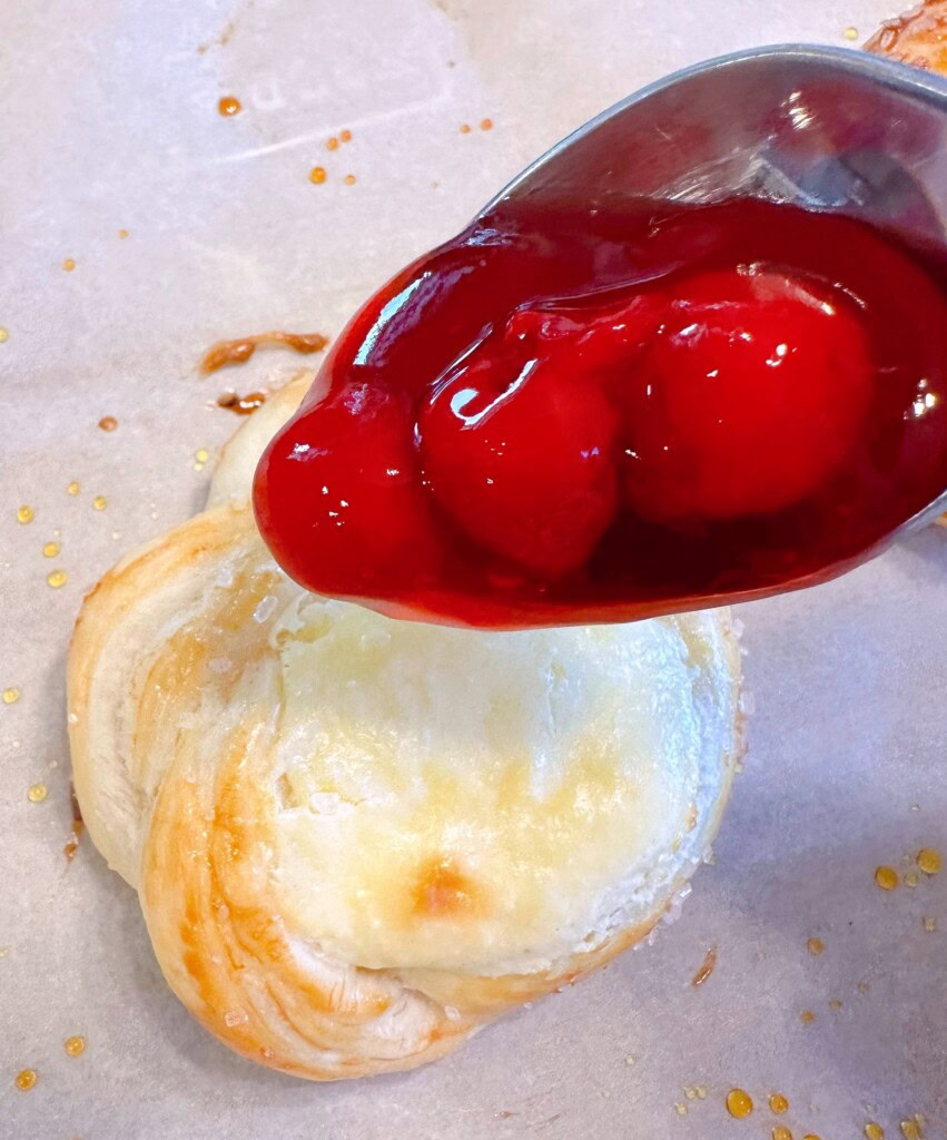 Adding three cherries to the top of each Danish on top of the cream cheese.