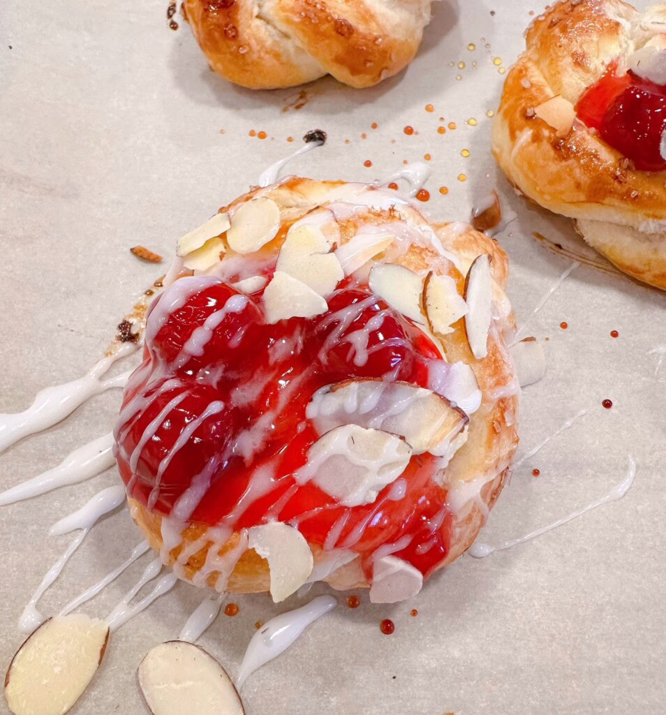 Drizzling icing over cherry danishes and adding sliced almonds.