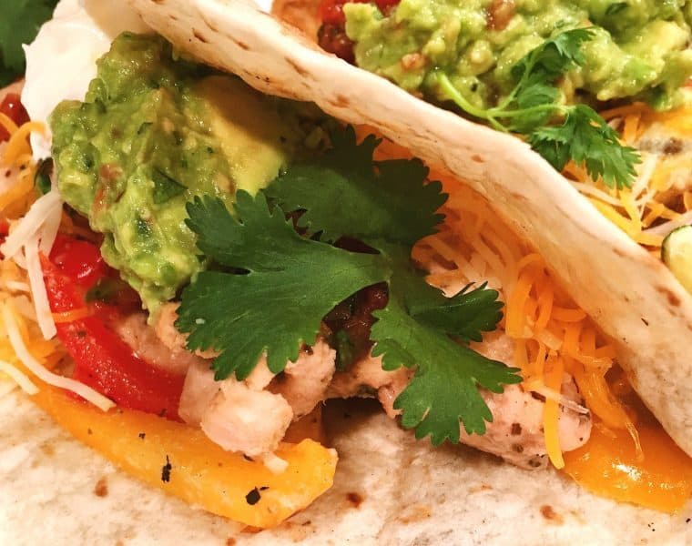 a folded tortilla with chicken, cheese, cilantro, avocado and tomatoes