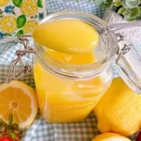 Lemon Curd on a spoon with lemons and strawberries.