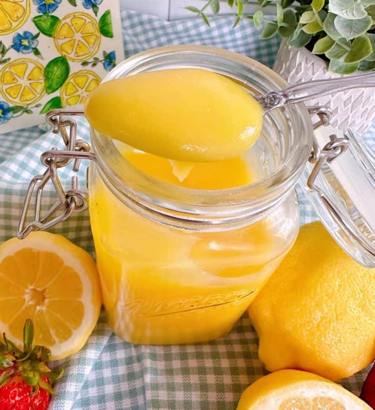 Lemon Curd on a spoon with lemons and strawberries.