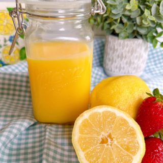 Homemade microwave lemon curd in a mason jar surrounded by lemons and fresh strawberries.