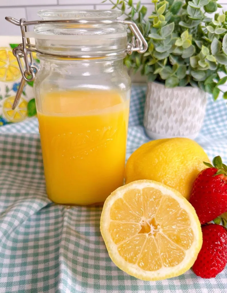 Homemade microwave lemon curd in a mason jar surrounded by lemons and fresh strawberries.