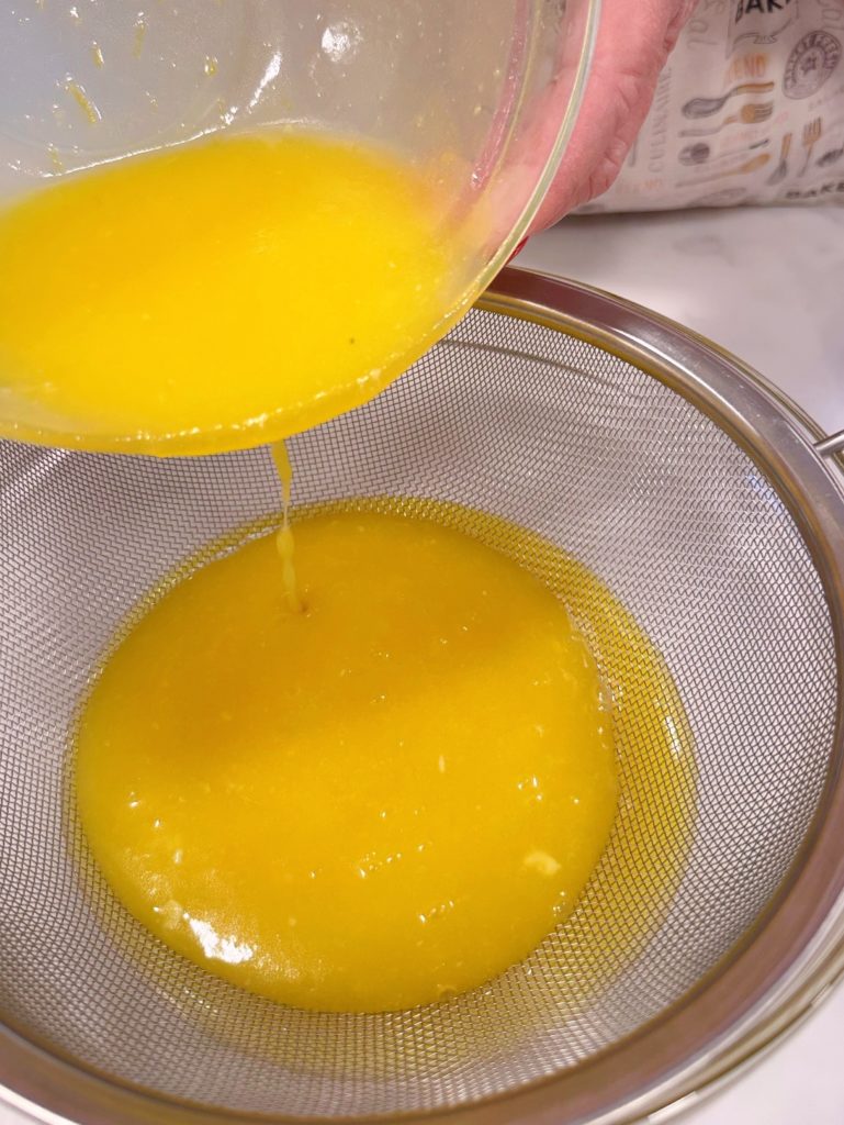 Pouring curd through a metal strainer.