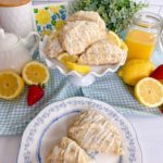 Lemon Poppy Seed Scones on a cake plate and extra's on a serving plate with lemons, strawberries, and fresh lemon curd.