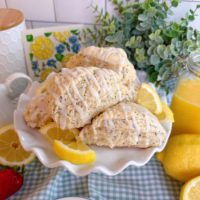 Lemon Poppy Seed Scones piled high on a cake plate with fresh lemon slices.