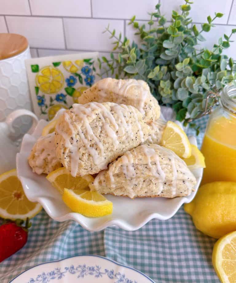 Lemon Poppy Seed Scones piled high on a cake plate with fresh lemon slices.