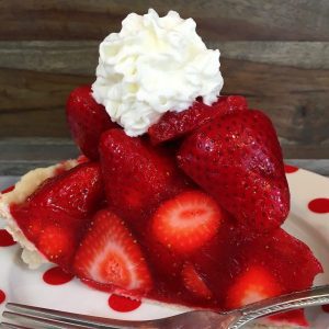 A slice of fresh strawberry pie with whip cream on top