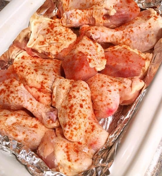 cut up chicken sprinkled with seasonings in a lined baking dish