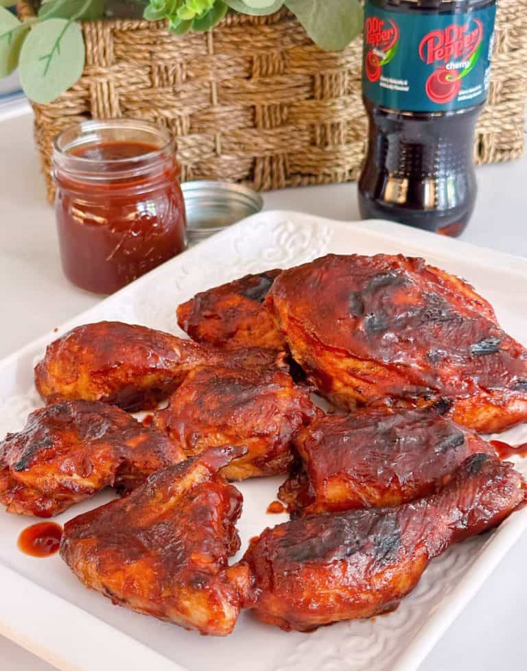 Perfectly grilled Cherry Dr Pepper Chicken on a white platter with more BBQ sauce in the background.