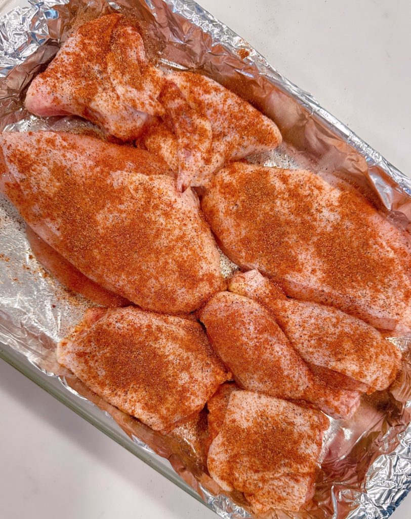 Chicken in foil lined baking pan and seasoned with seasonings.