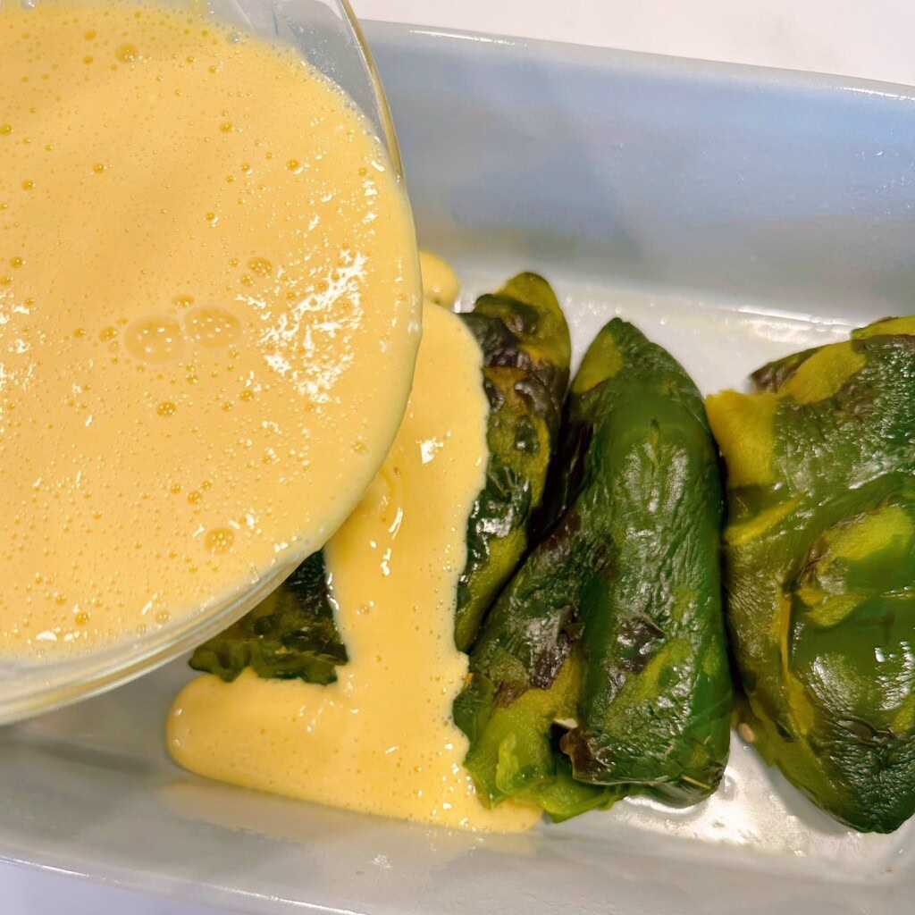 Batter being poured over stuffed chili peppers.