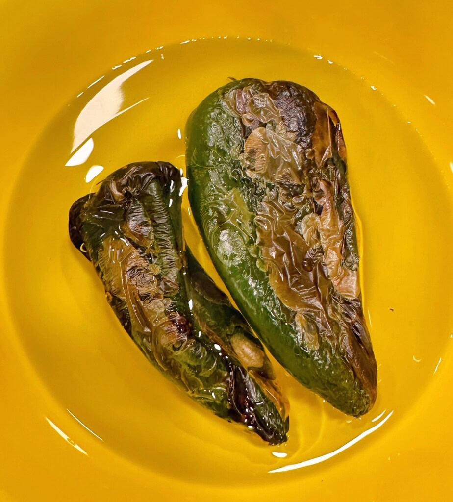 Roasted poblano peppers in water in a bowl.