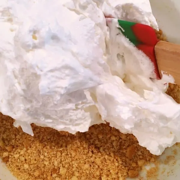 Crushed cookie crumbs and whipping cream being mixed together to create crust for Orange Creamsicle Frozen Dessert