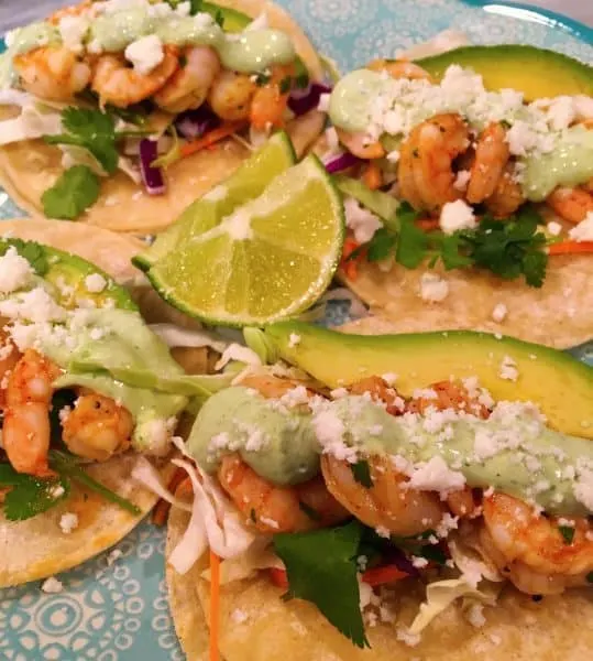 four shrimp tacos with crema sauce and sliced avocado