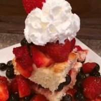 A slice of shortcake made with strawberries, blue berries and raspberries with whipped cream on top