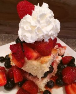 A slice of shortcake made with strawberries, blue berries and raspberries with whipped cream on top