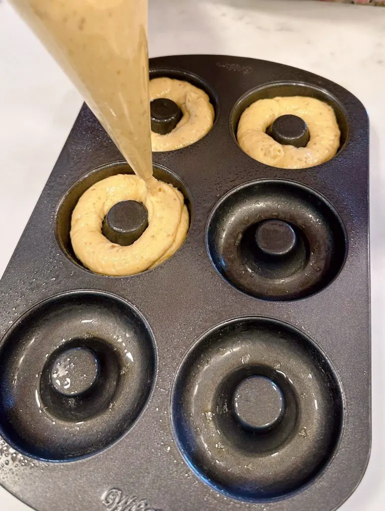 Piping dough into donut pans.
