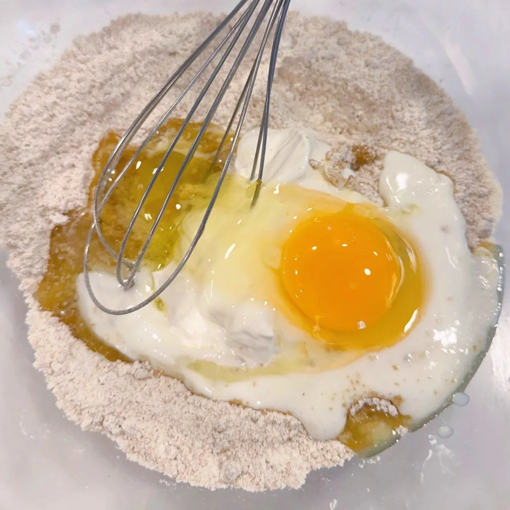 Adding wet ingredients to the dry donut ingredient batter.
