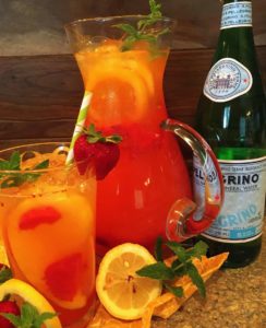 Mango Strawberry Lemonade in a pretty pitcher with sparking water bottle.