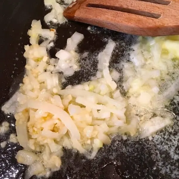 Onions and garlic being sauteed in a frying pan with olive oil