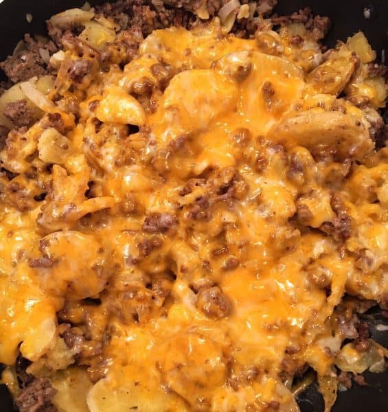 Ground beef, potatoes, and melted cheese in a large skillet on top of the stove.