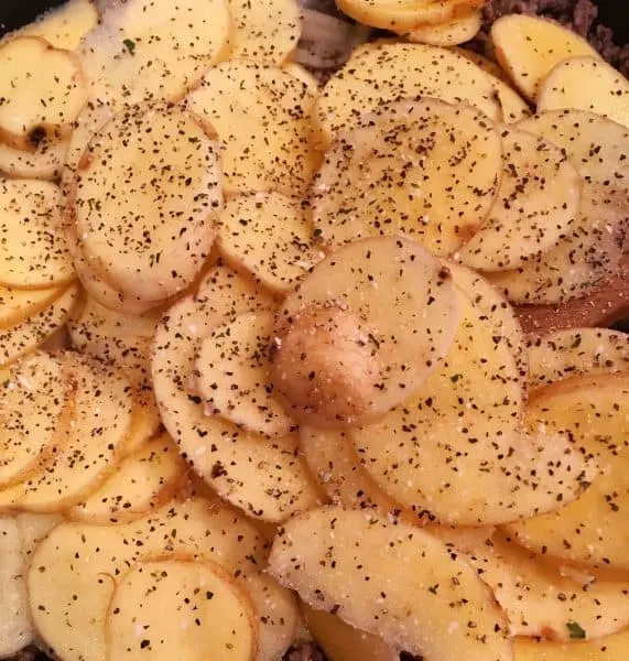 Sliced potatoes with salt and pepper in skillet with hamburger meat