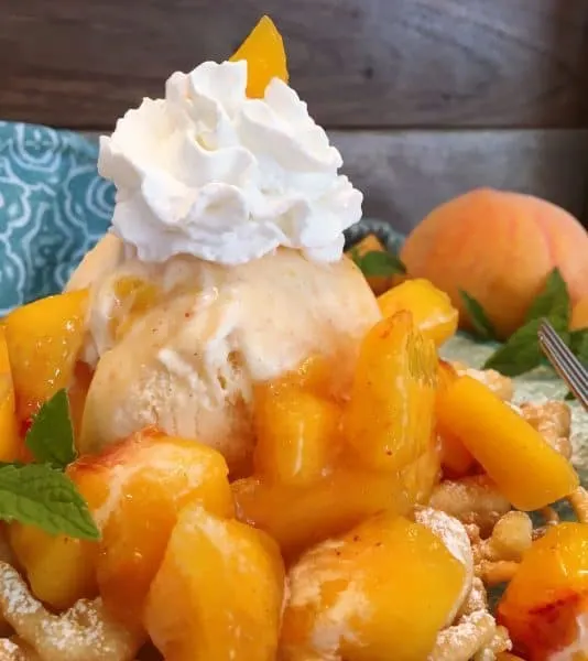 Homemade funnel cake topped with a scoop of ice cream and fresh cut up peaches