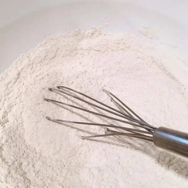 Flour and other dry ingredients in a bowl being whisked together.