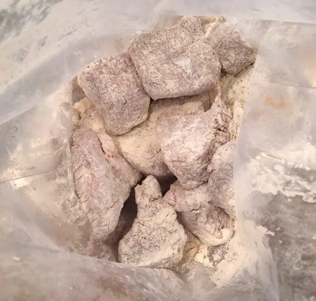 Chunks of beef being tossed in a bag with flour