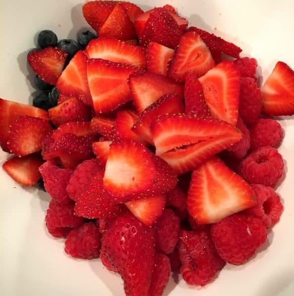 Strawberries, blueberries, and raspberries cut up in a bowl