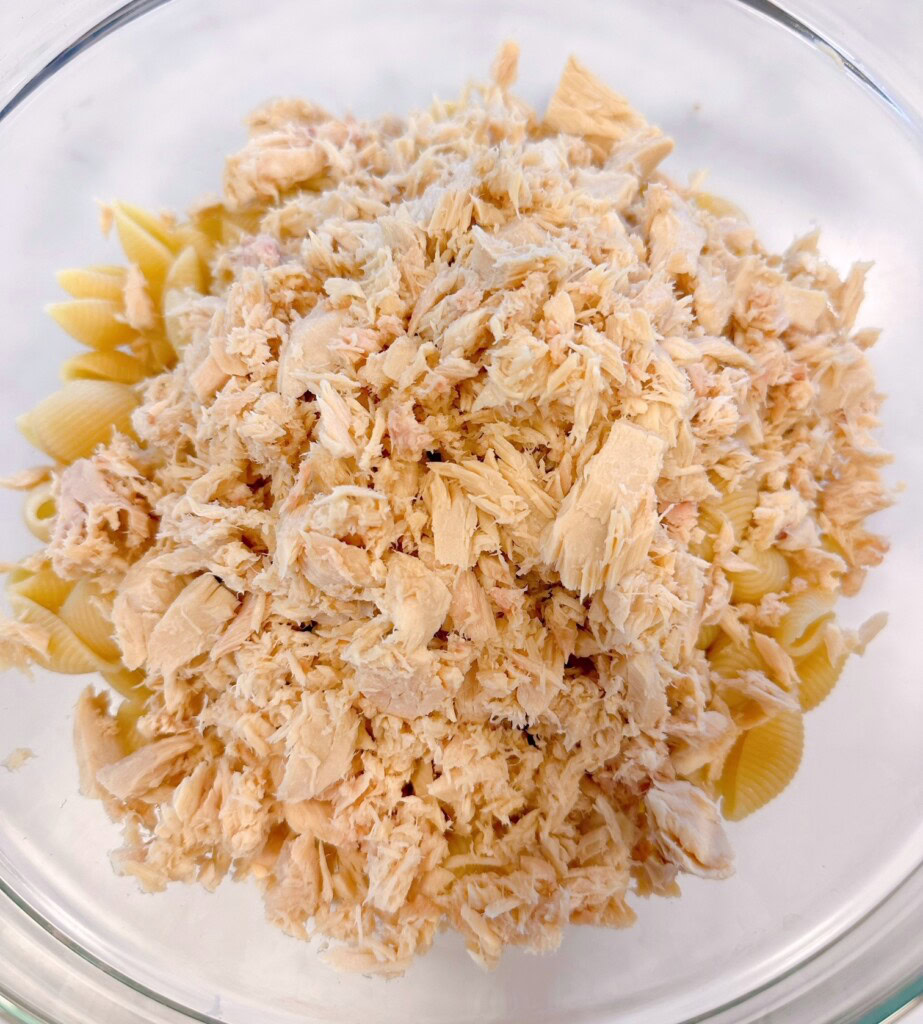 Adding Tuna to the Noodles in the mixing bowl.
