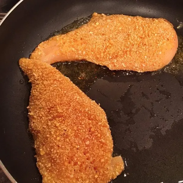 chicken breast coated and frying in skillet