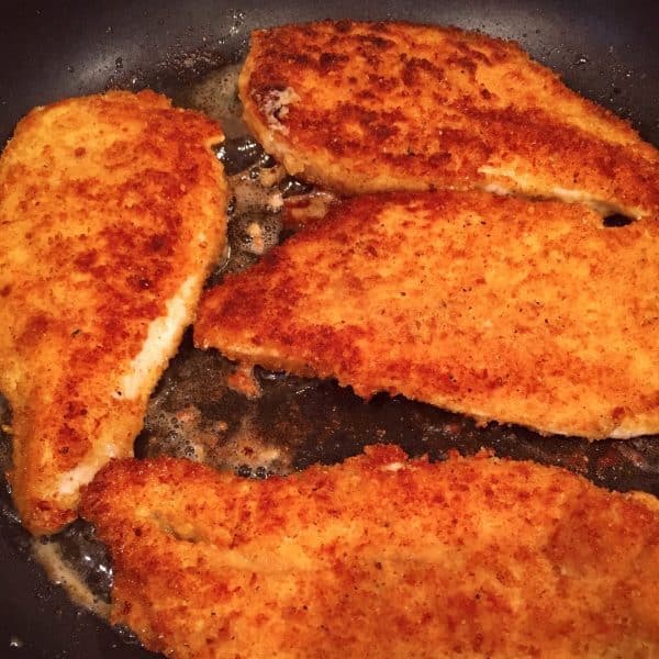 fried chicken breast in skillet turned over 